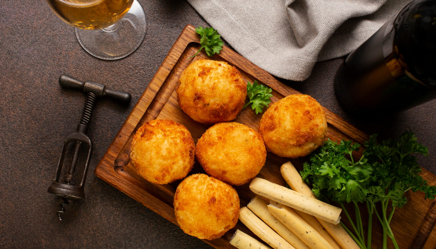 Закусочные шарики из крабовых палочек на сервировочной доске рядом со штопором и вином