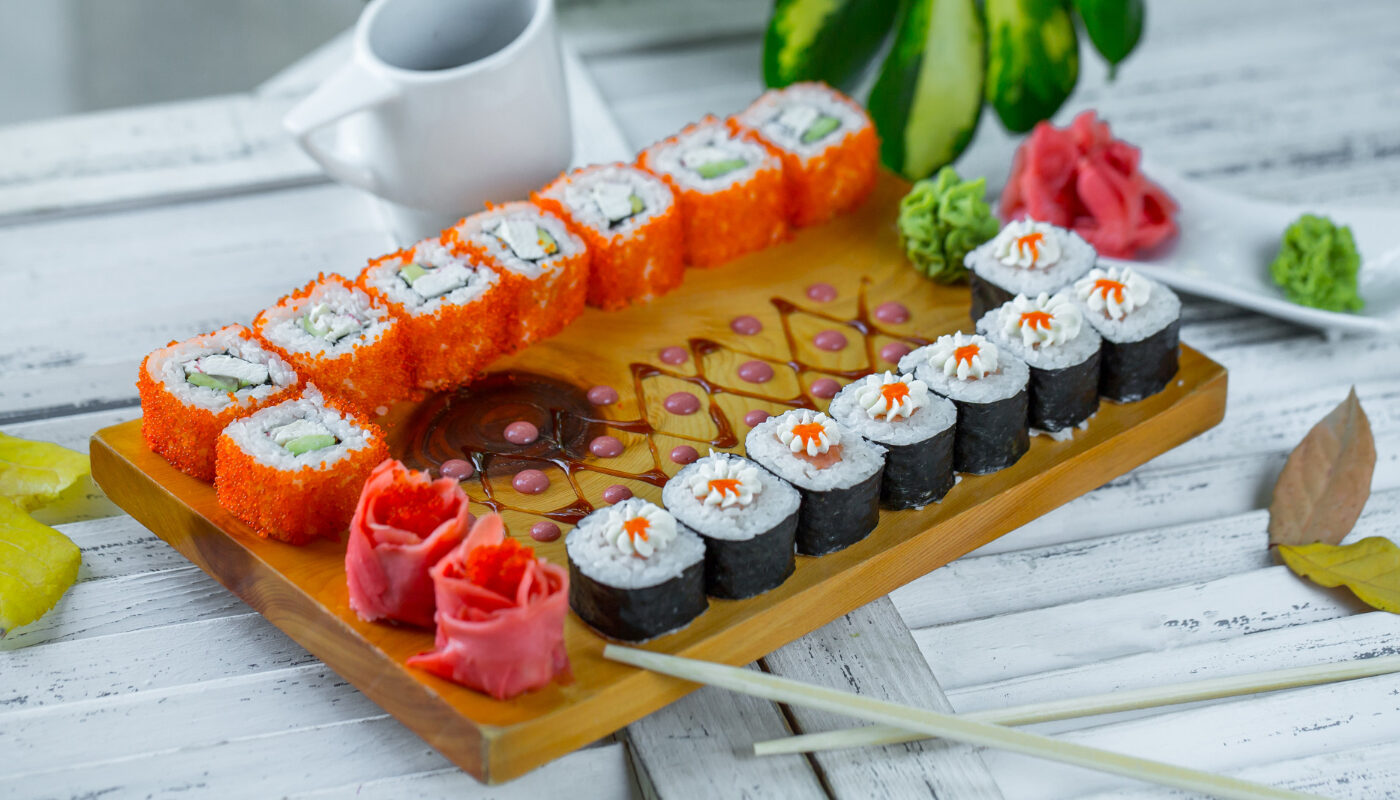 суши на деревянной доске с имбирем и палочками